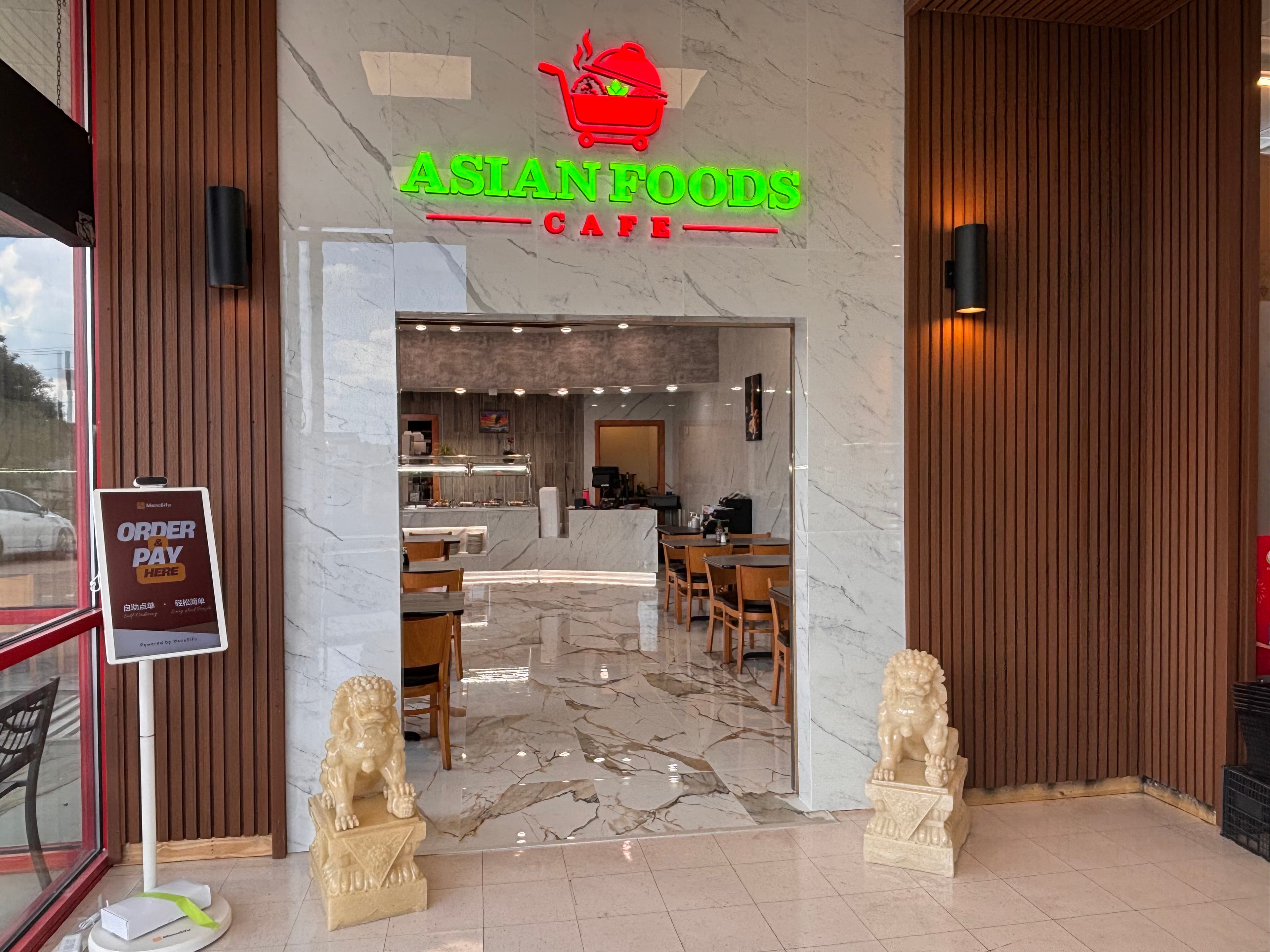 The Asian Foods storefront in Tupelo, with a lit sign above the entrance and stone guardian lions either side of the door